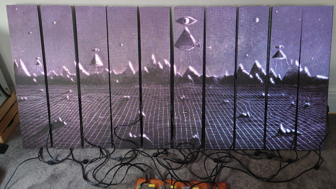 10 identical LED panels lined up leaning against a wall with a surreal image displayed and power cables showing