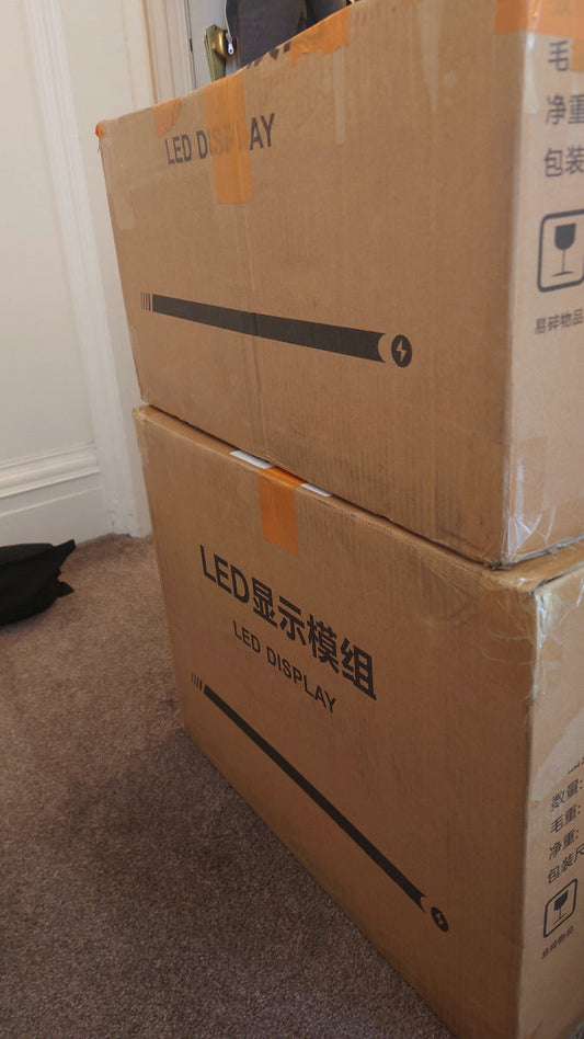 Two stacked boxes with LED DISPLAY written on the side sat on a carpeted floor