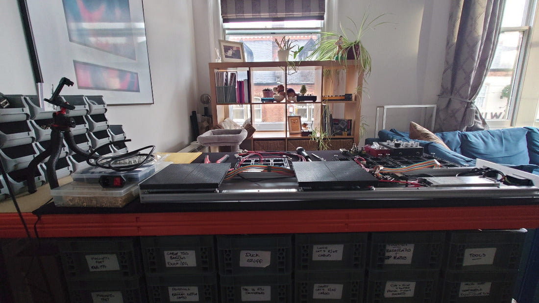 A workbench with parts bins underneath it and a shelving unit in the background