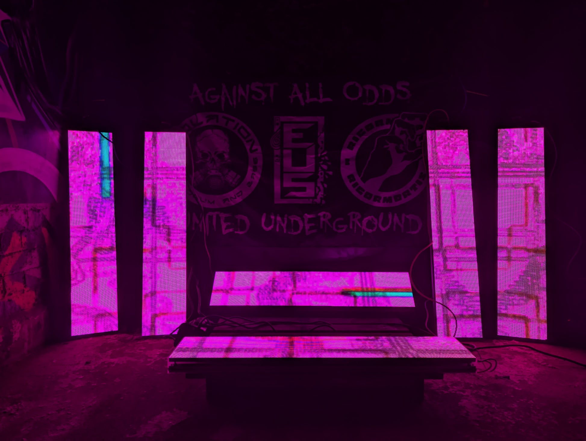 6 LED panels arranged against a wall glowing pink with glitchy visuals on a concrete floor