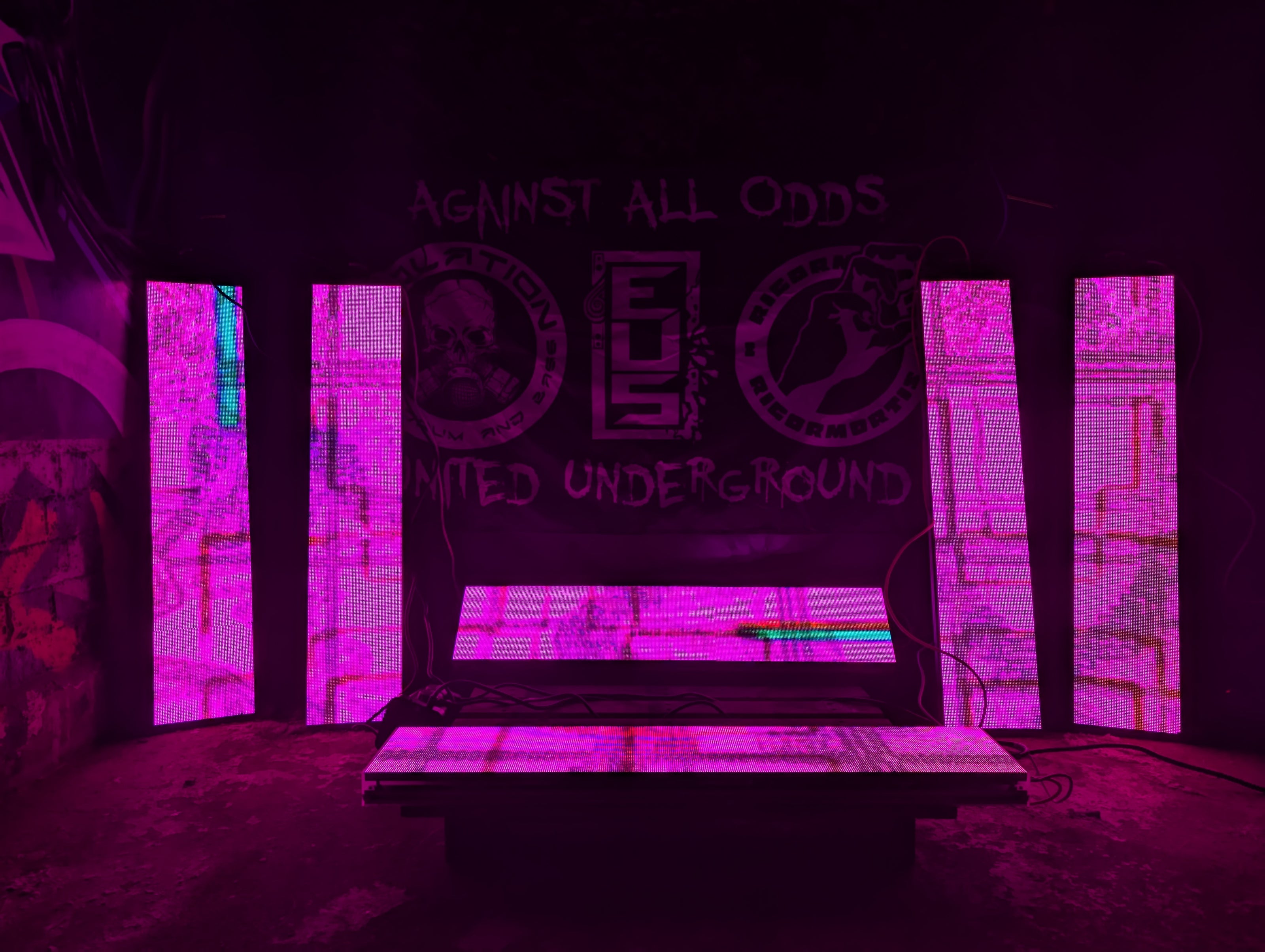 6 LED panels arranged against a wall glowing pink with glitchy visuals on a concrete floor