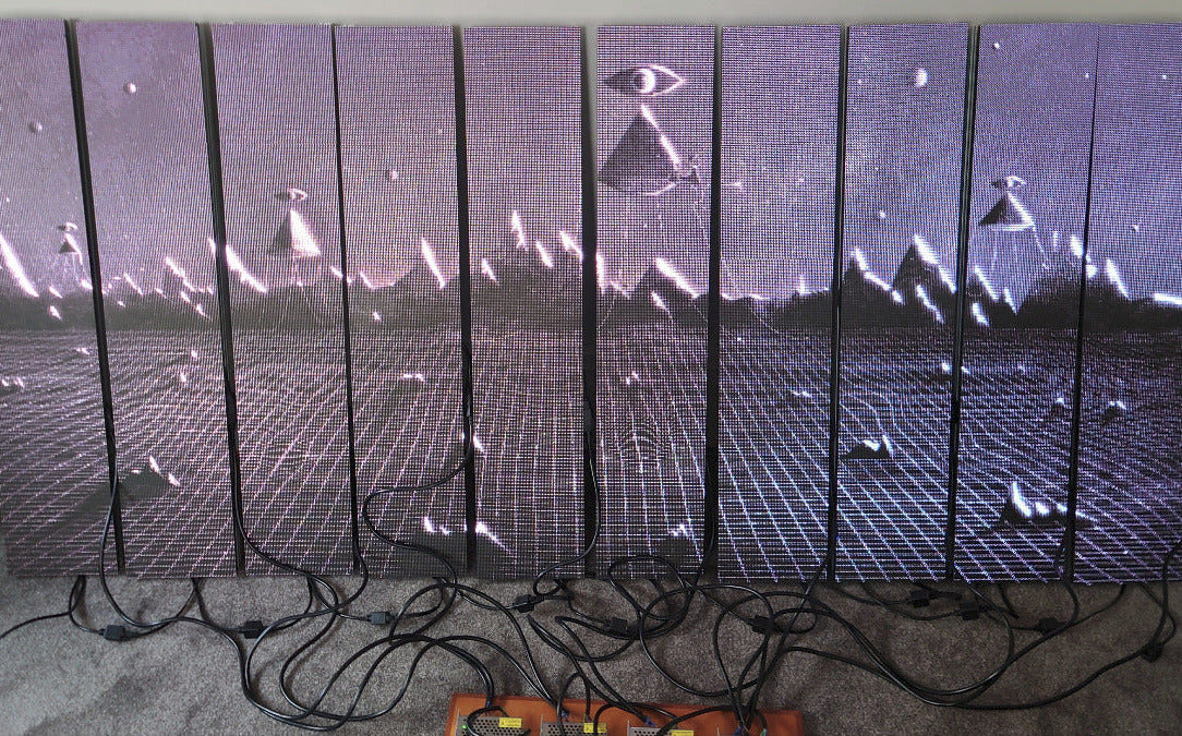 10 identical LED panels leaning against a wall with a black and white surreal image displayed and power cables on floor 