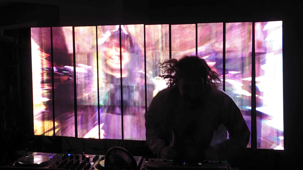 Person playing DJ equipment with colorful abstract projections on a screen behind them
