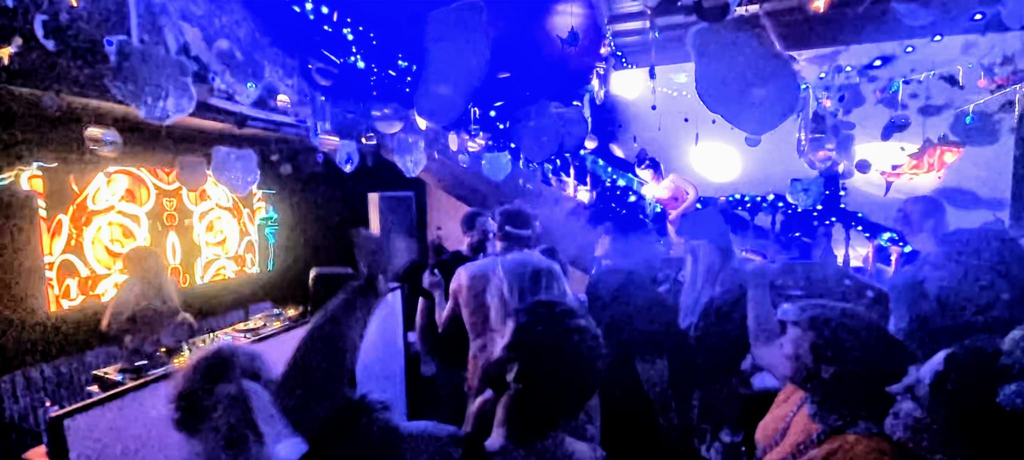 Crowd of people dancing in a small venue to a DJ with bright decor