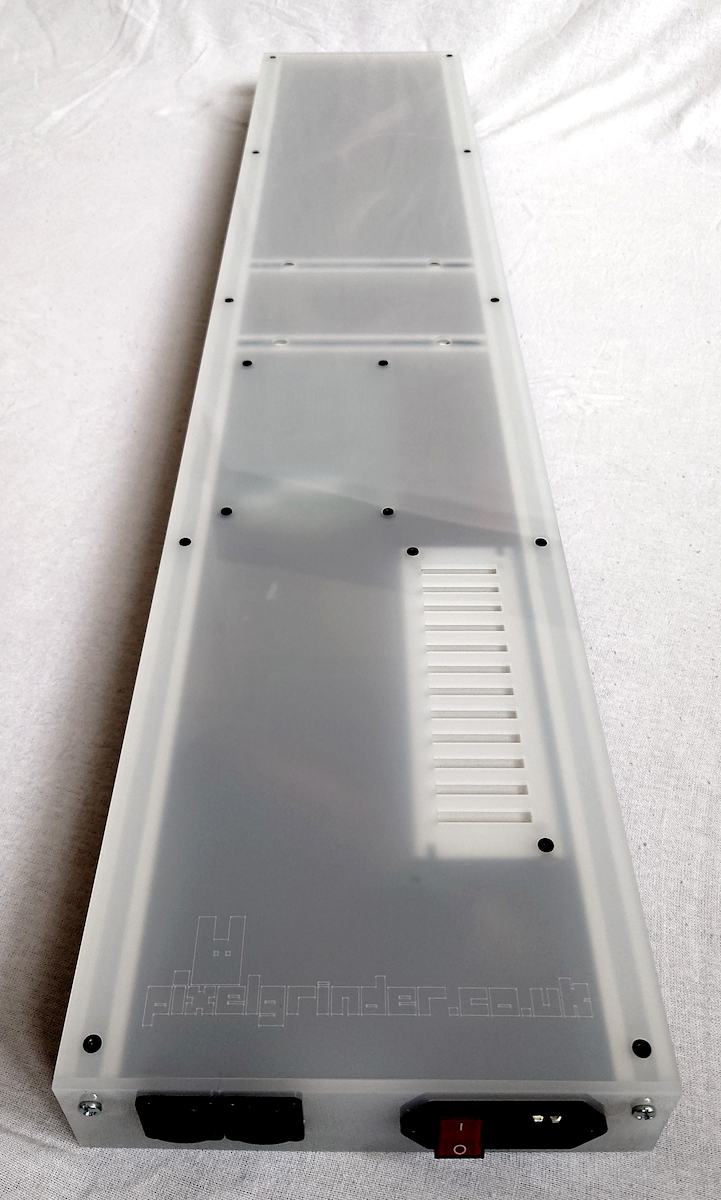 A long, narrow translucent white plastic LED panel back plate with mounting holes, a vented slot, and small black components at the bottom, photographed on a white fabric surface.