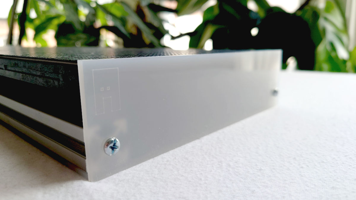 A close-up of the acrylic top plate of an LED panel, resting on a white textured surface with a blurred background of green foliage.
