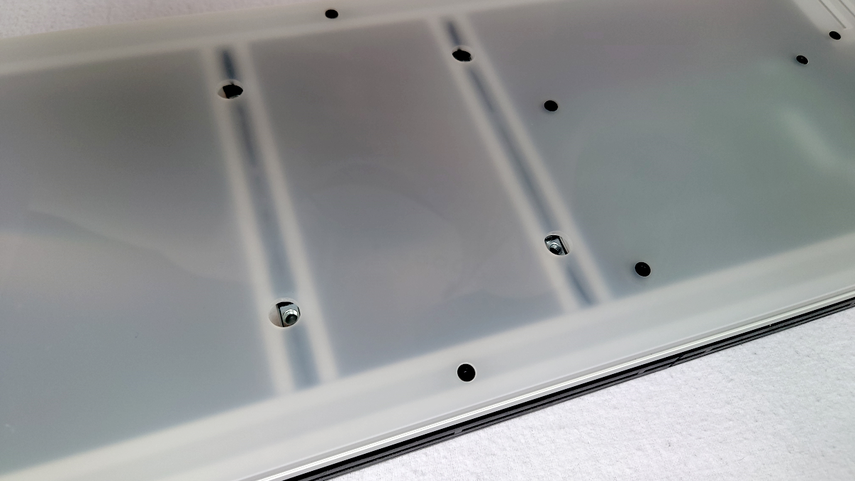 Close-up of a translucent white acrylic panel with pre-drilled VESA mounting holes, shown on a light textured surface.