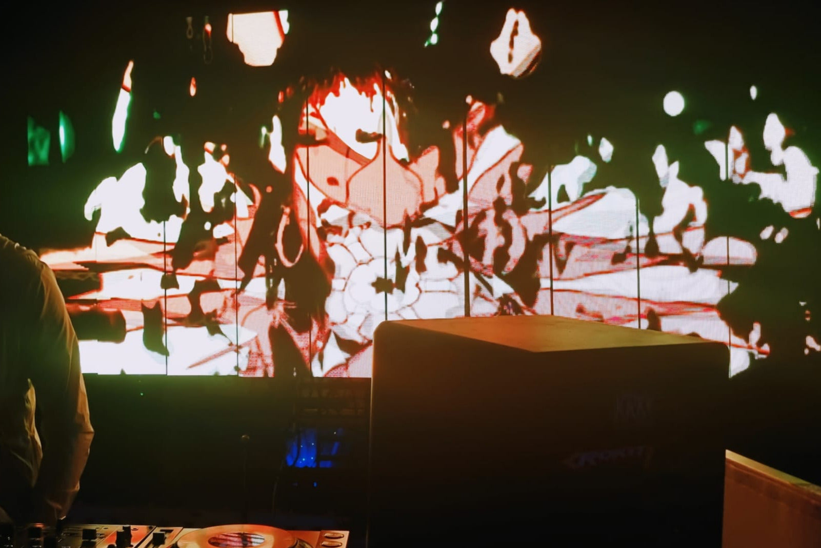 DJ standing in front of a large LED screen displaying abstract visuals in a dark setting