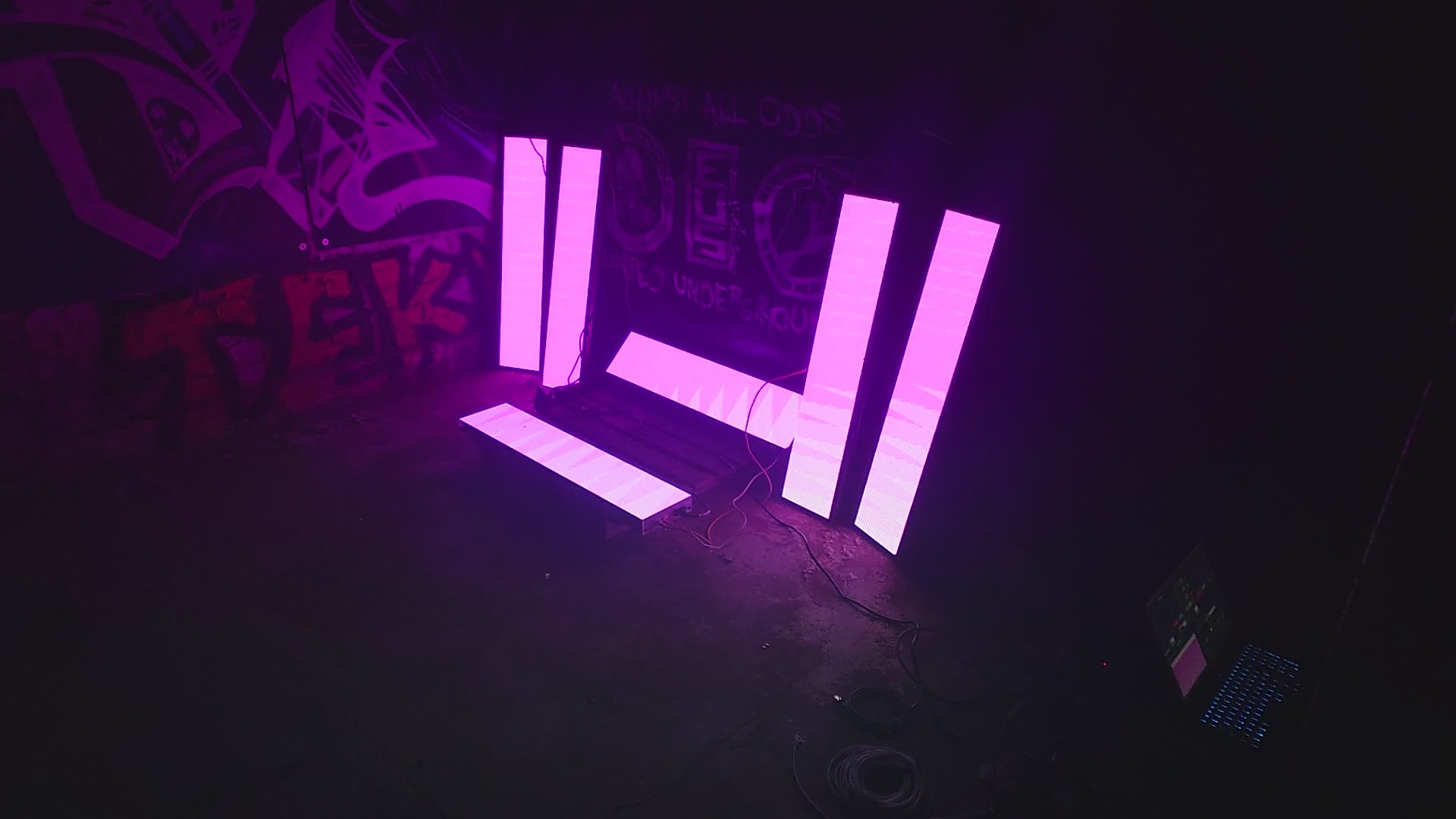 Load video: 6 LED panels in a warehouse with graffiti on the wall they are leaning against, flashing pink
